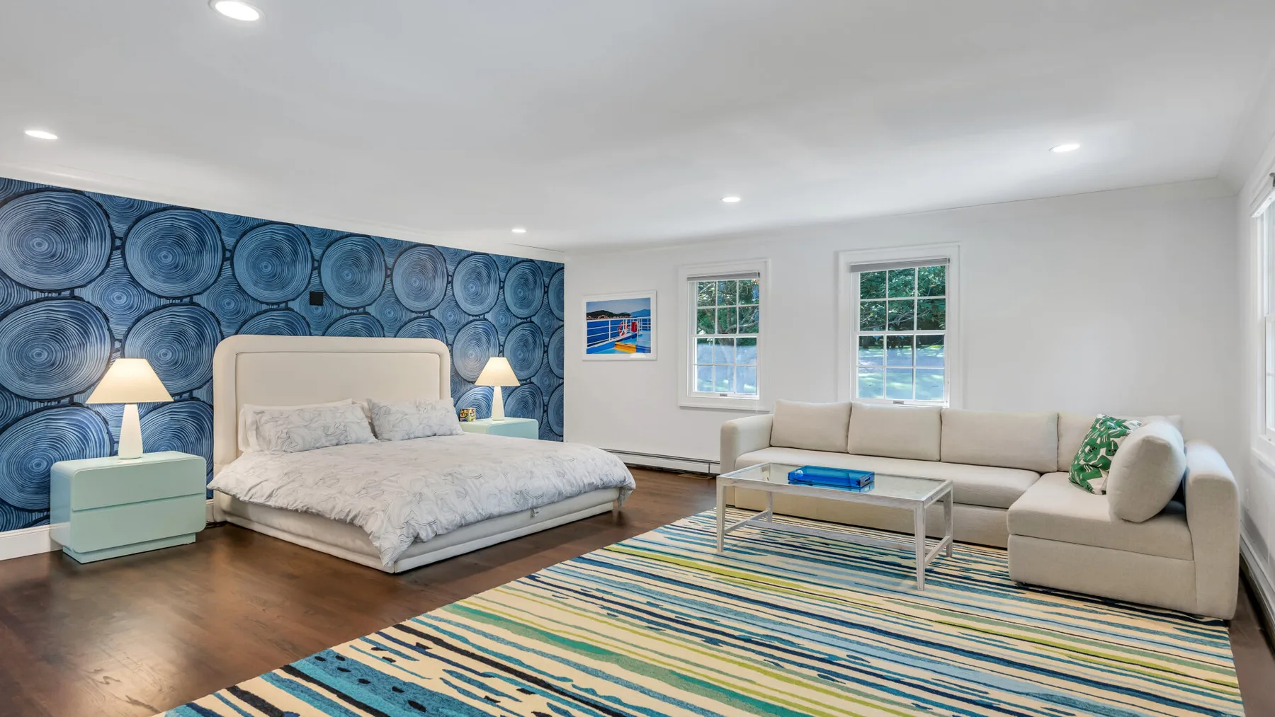 A bedroom with a bed, seating area, and blue patterned accent wall.