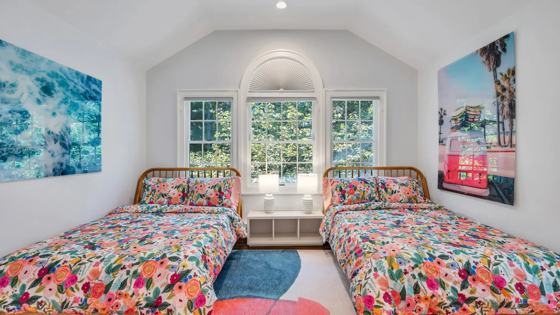 A bright bedroom with two beds covered in colorful floral bedding.