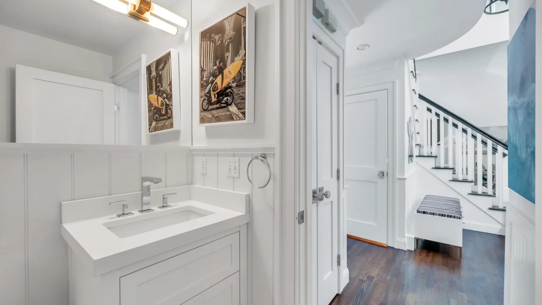 A bathroom vanity opens onto a bright hallway with a staircase.