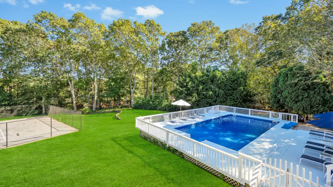 An outdoor swimming pool and tennis court sit beside a broad green lawn.