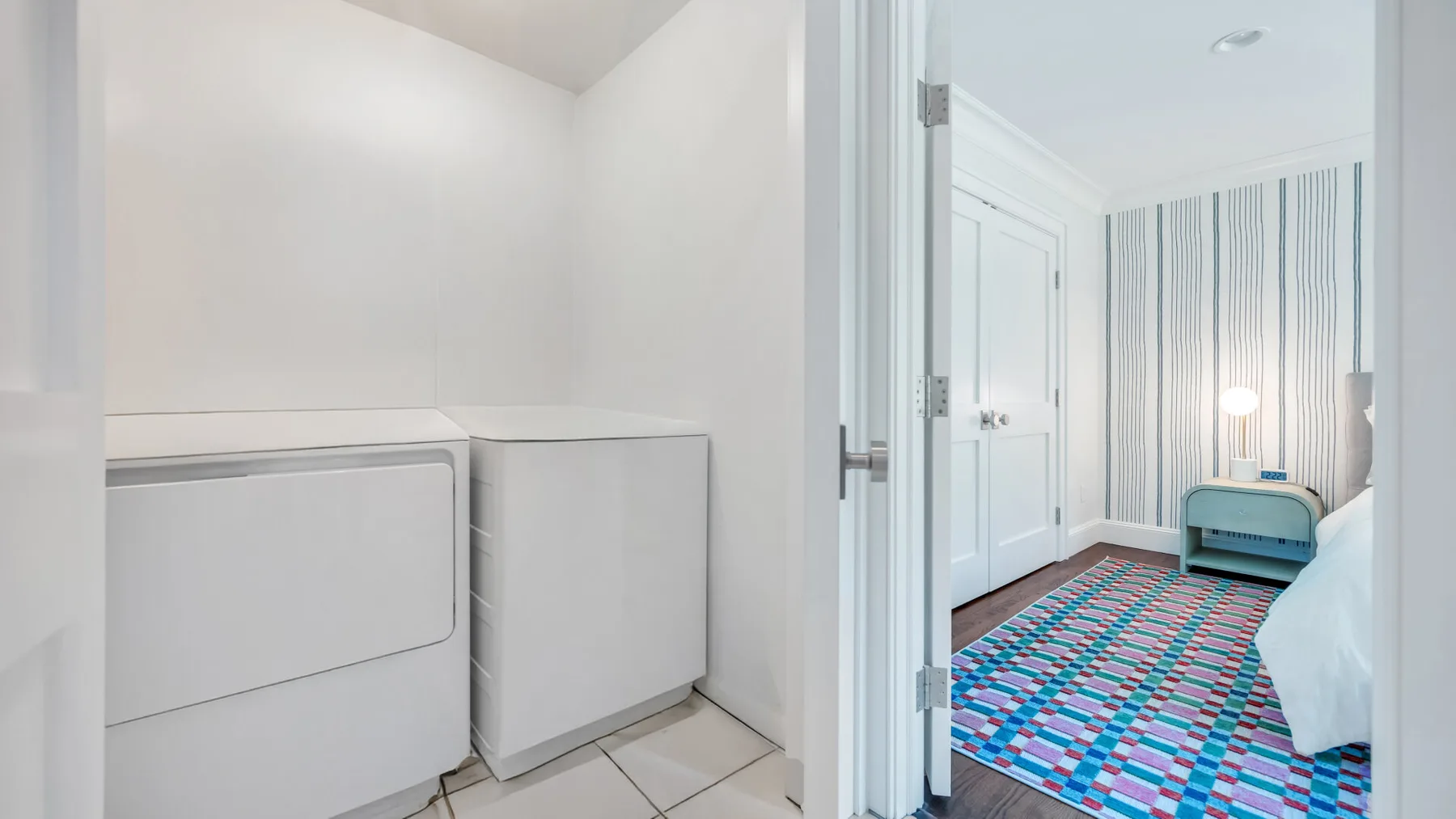 A laundry area opens onto a bedroom with striped walls and a colorful rug.