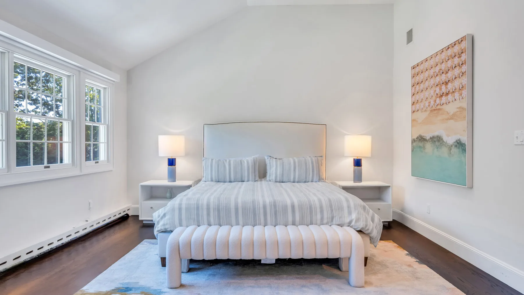 A bright bedroom with a neatly made bed and large windows.