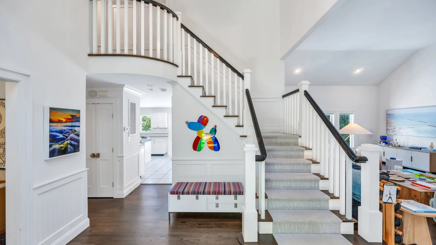 A bright interior with a curved staircase, a small bench, and an open kitchen.