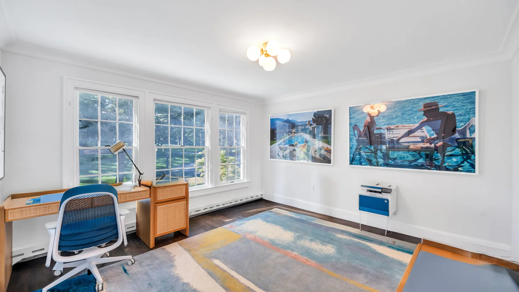 A bright room with a desk, large windows, and colorful artwork on the walls.