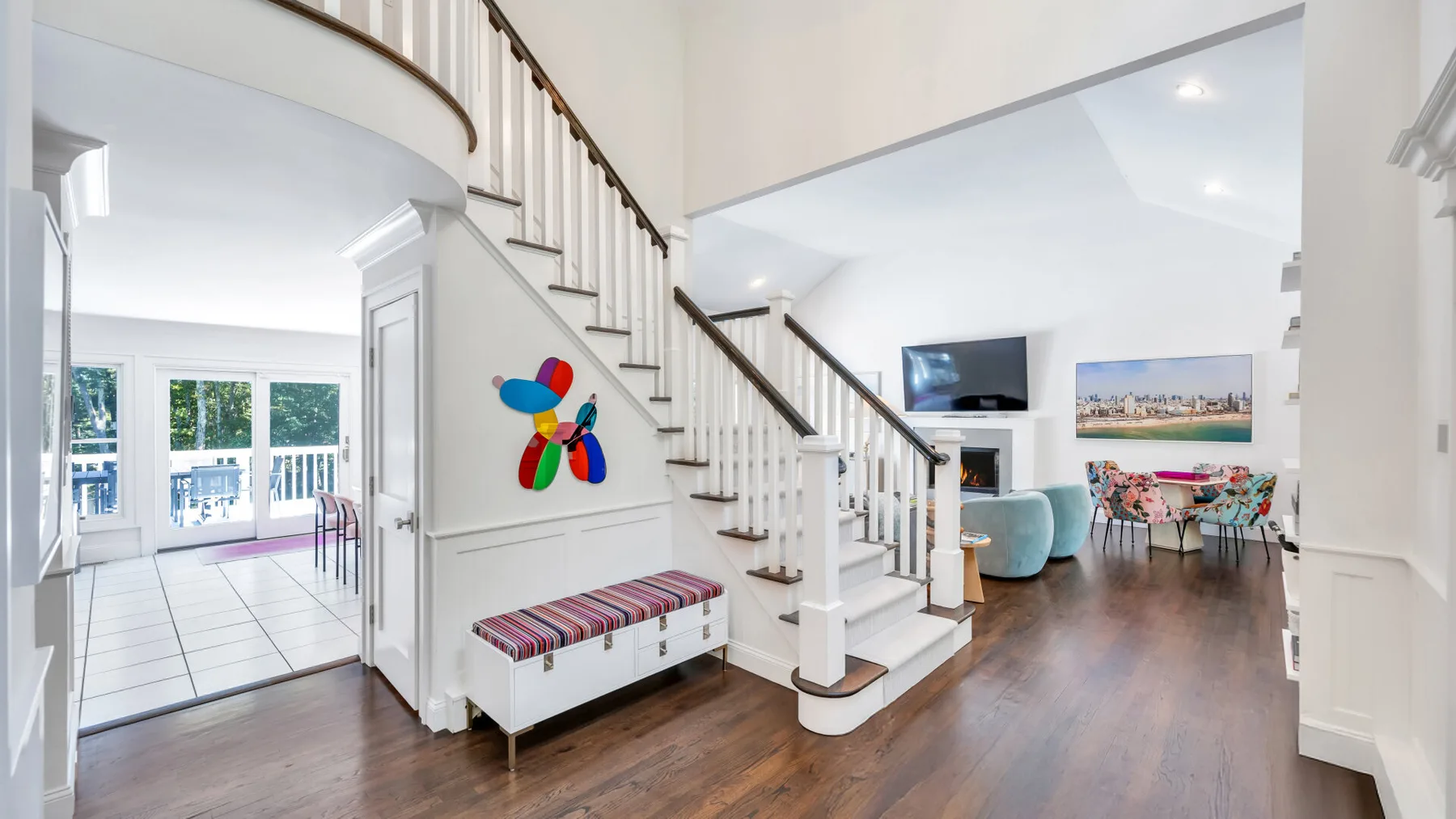 A bright living area with a staircase, colorful wall decor, and an adjoining dining space.