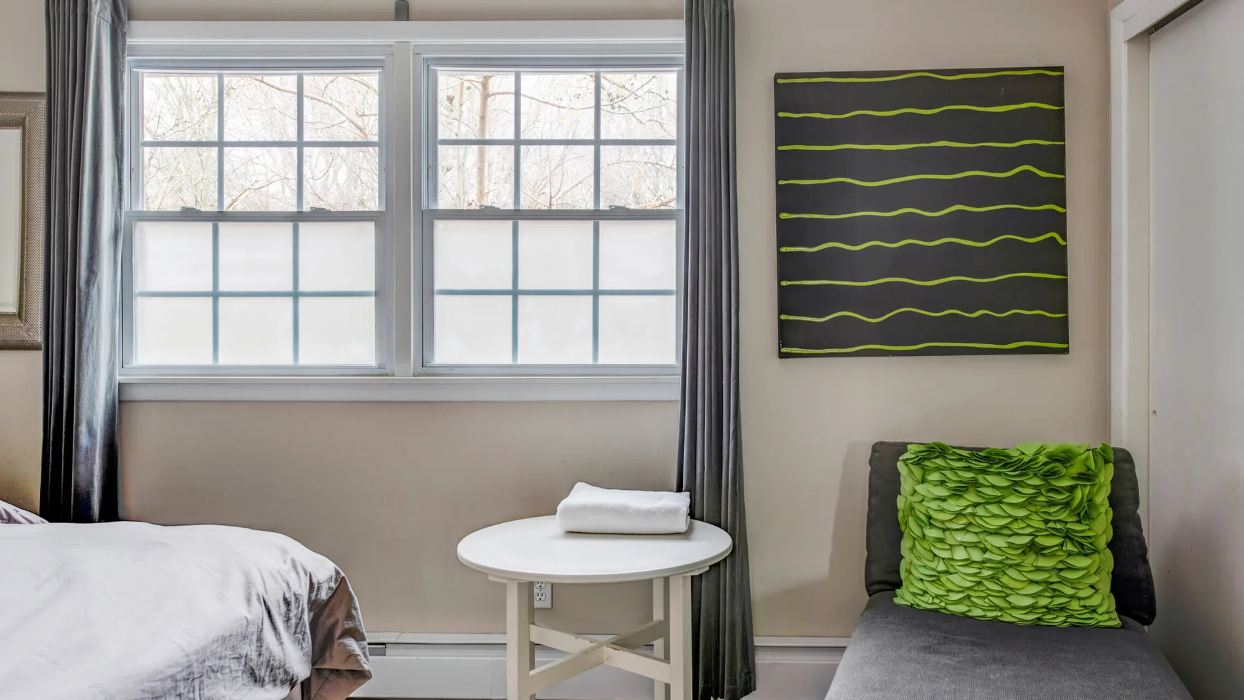 A bedroom with a bed beside two windows and a small round table.