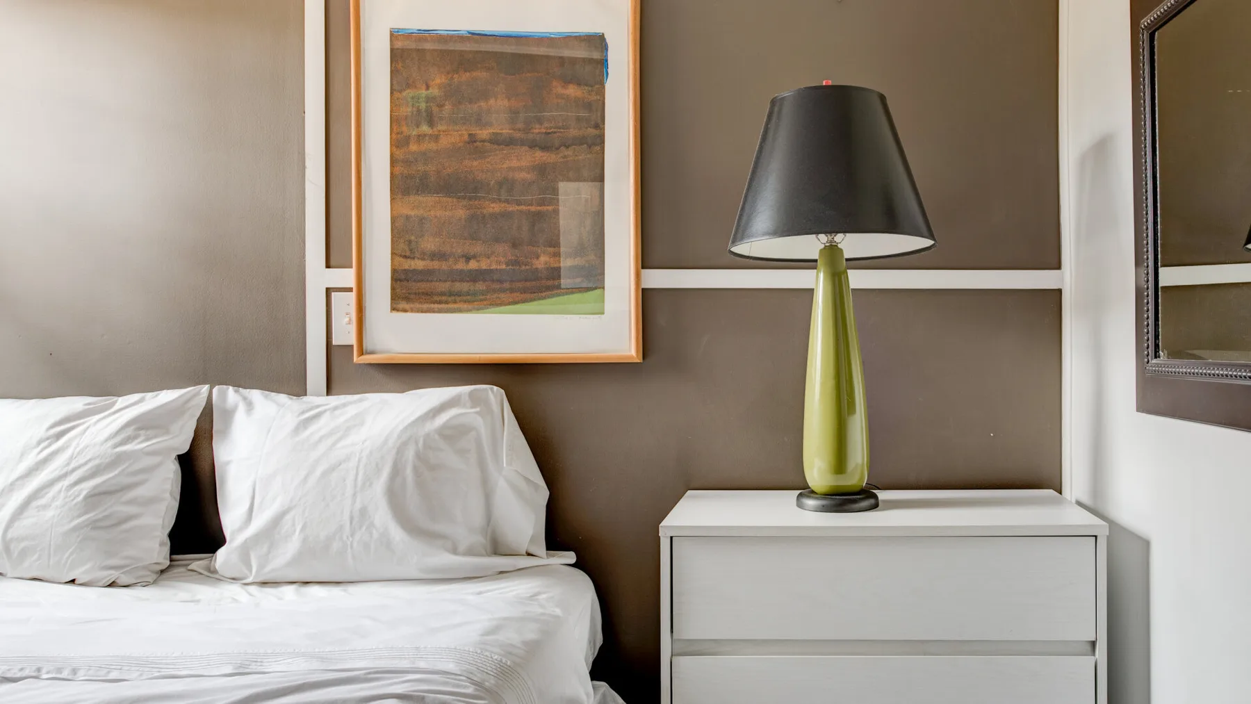 A bedroom with white bedding and a lamp on the bedside table.