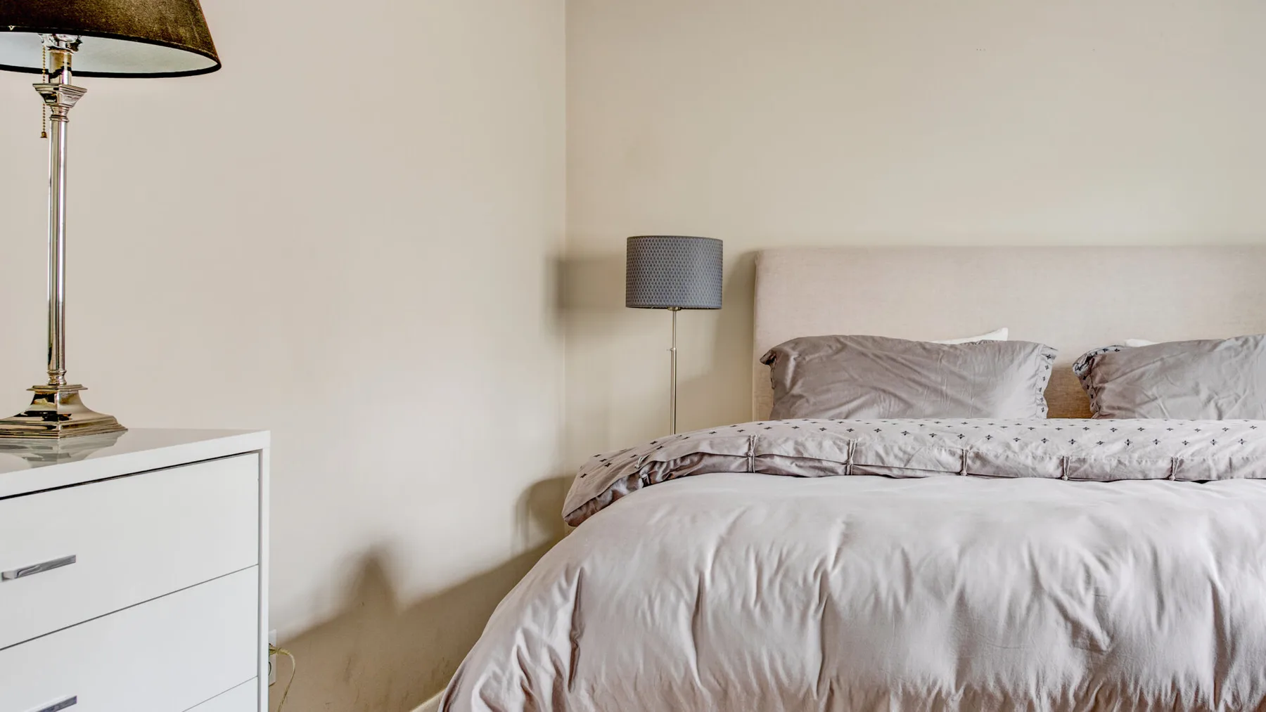 A bedroom with a bed dressed in pale patterned bedding.