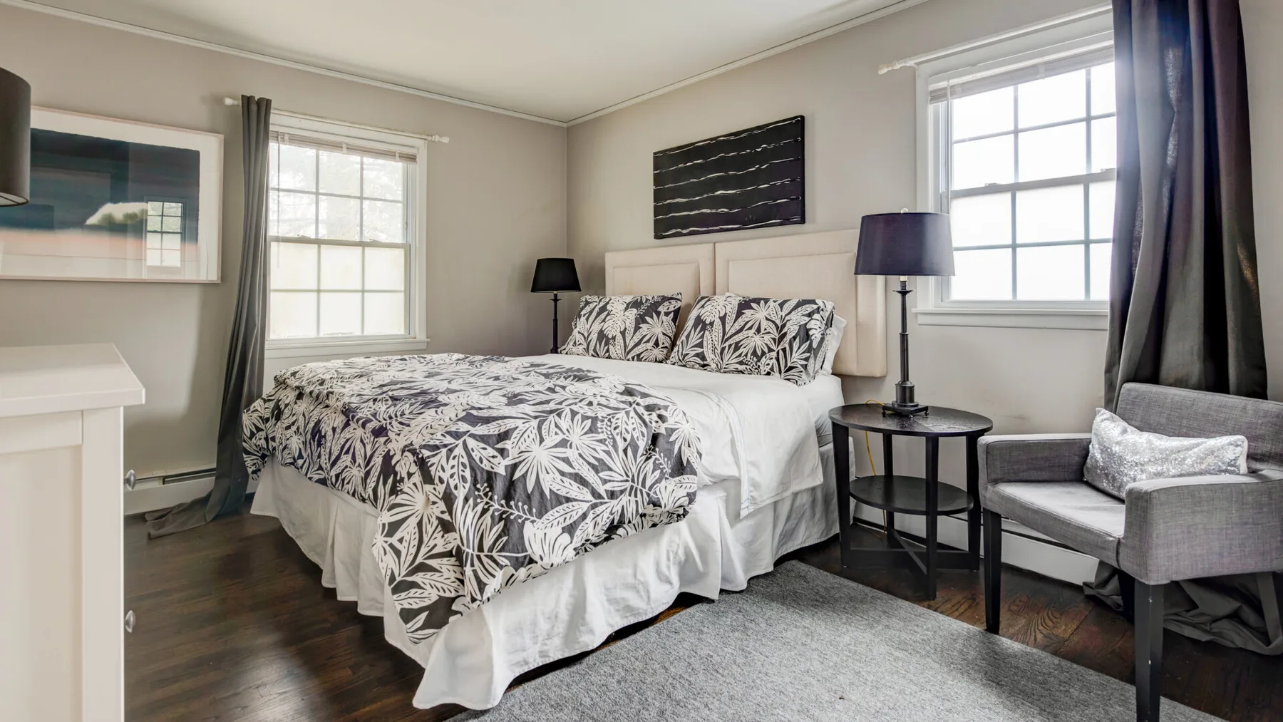 A bedroom with a bed, patterned bedding, and a small seating area by the window.