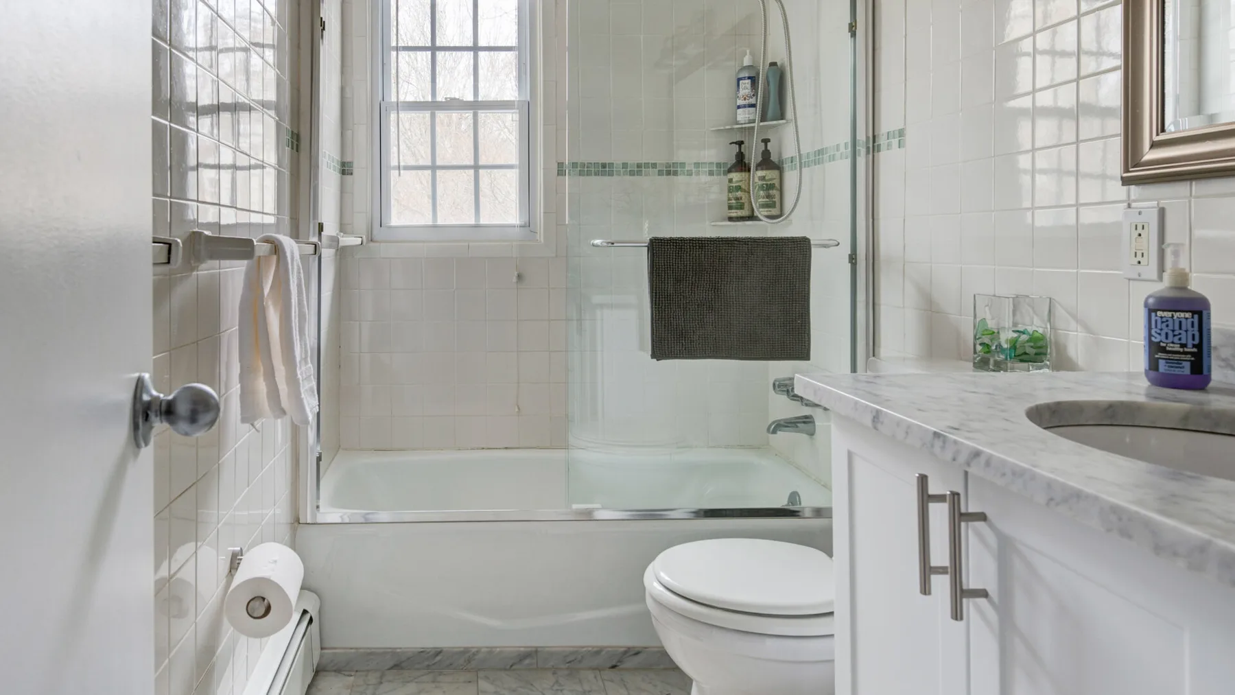 A bright tiled bathroom with a bathtub, shower, and sink.