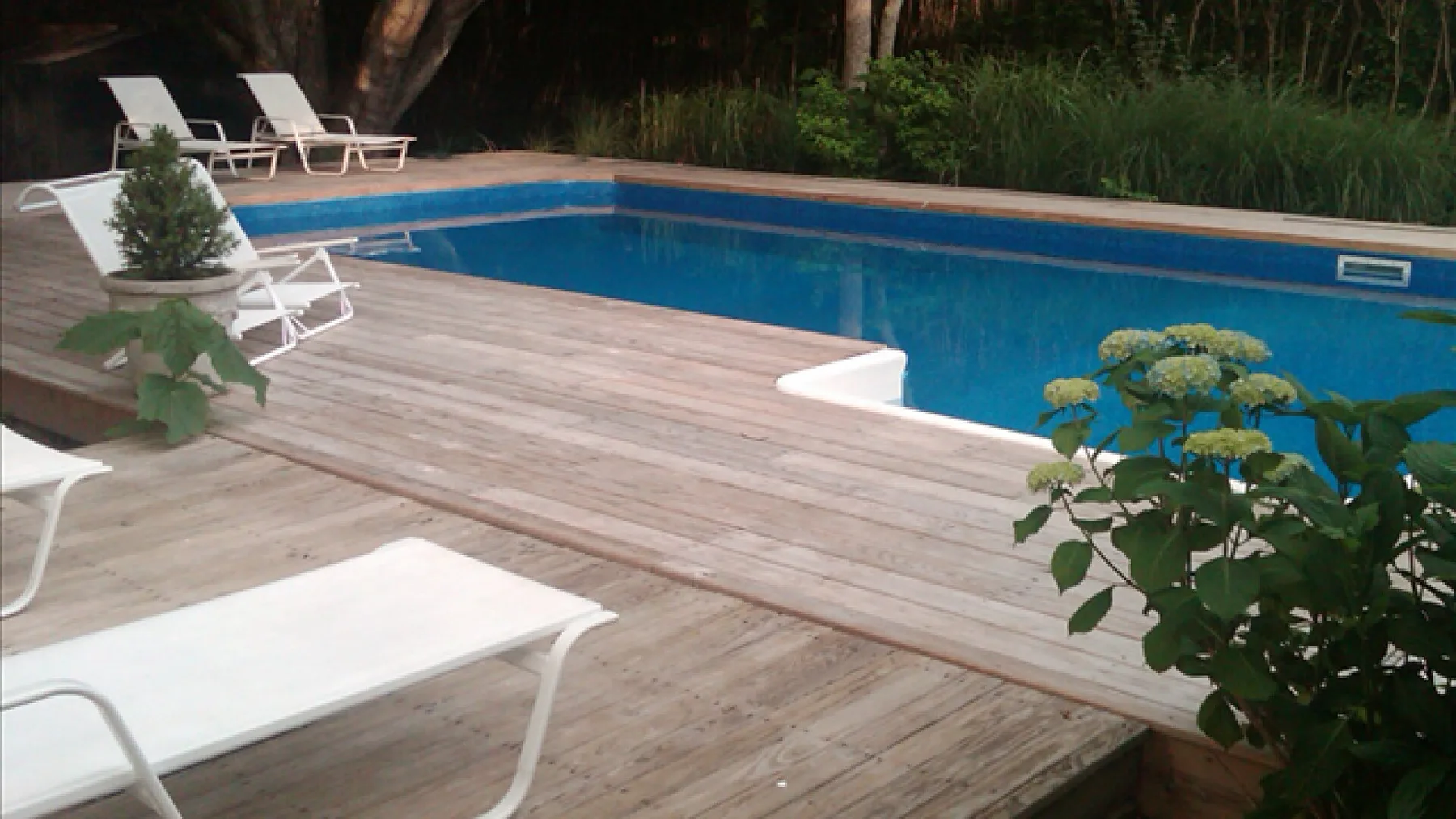 An outdoor swimming pool bordered by a wooden deck and lounge seating.