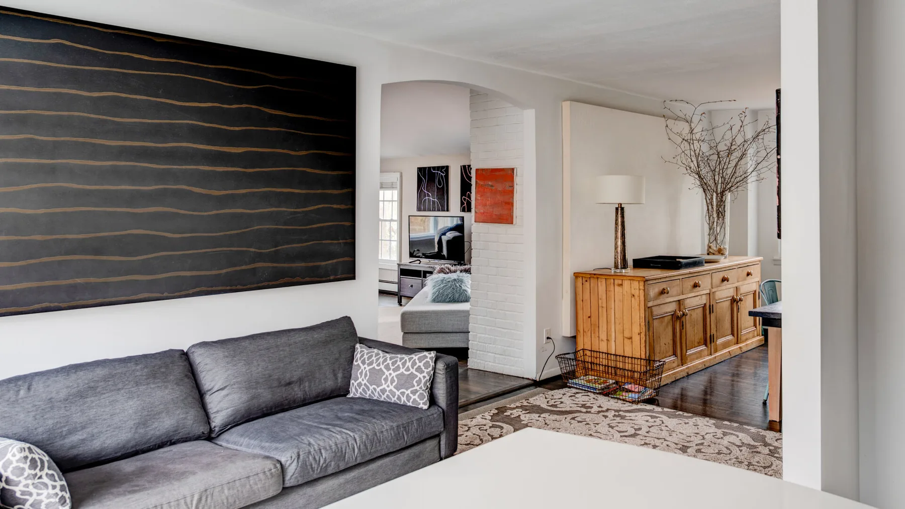 A living room with a gray sofa, large wall art, and a wooden sideboard.