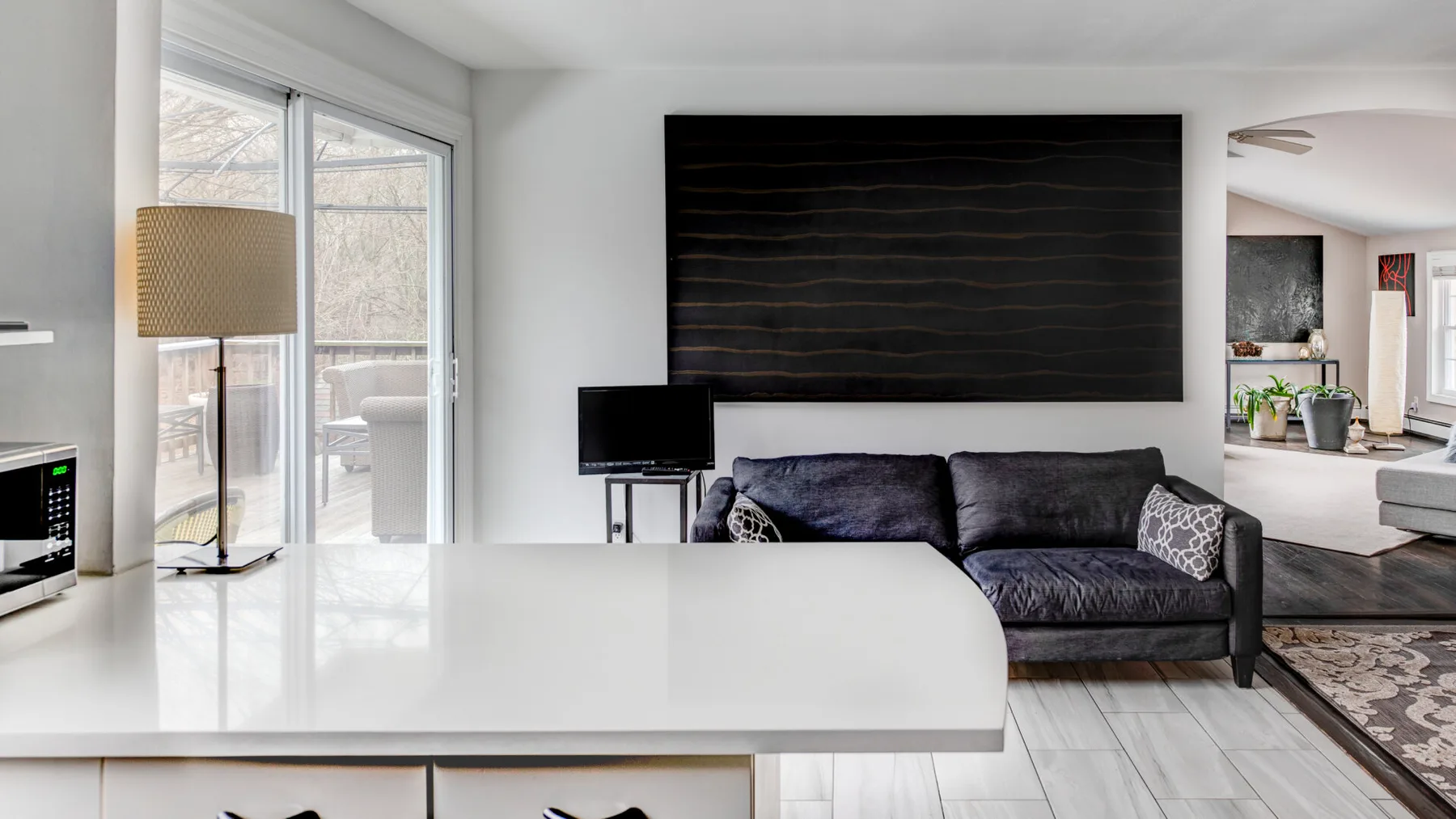 A bright living room with a dark sofa behind a broad white kitchen counter.