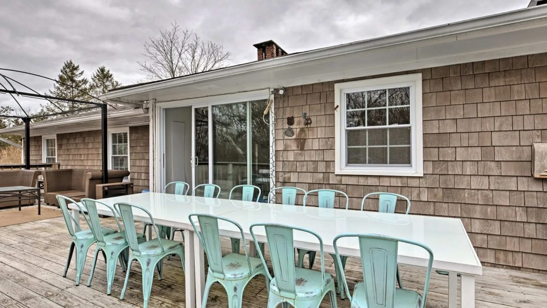 An outdoor dining area has a long table and pale blue seating beside the house.