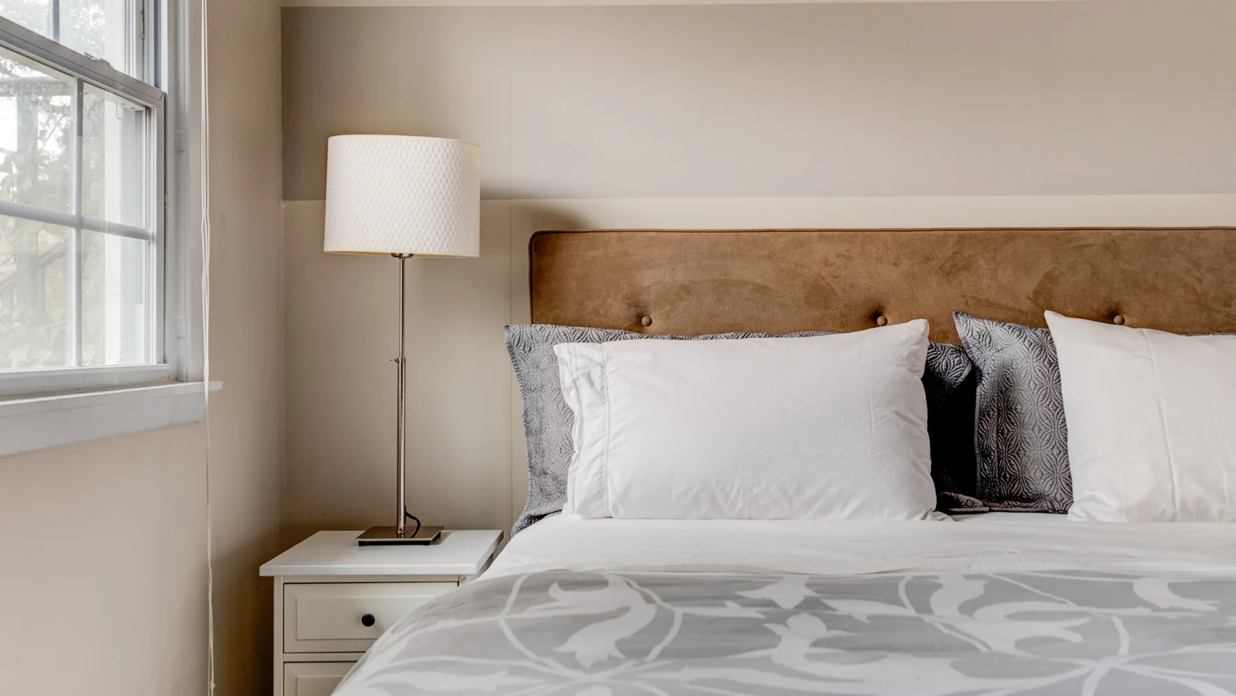 A bedroom with a neatly made bed, patterned bedding, and a bedside lamp.