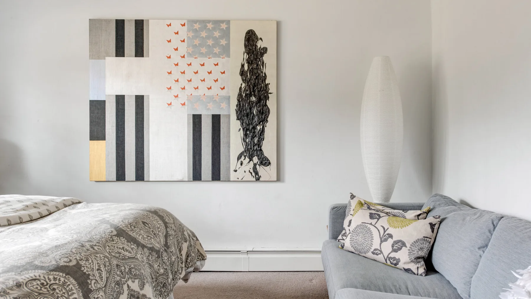 A bedroom with a patterned bedspread and a gray sofa beneath wall art.