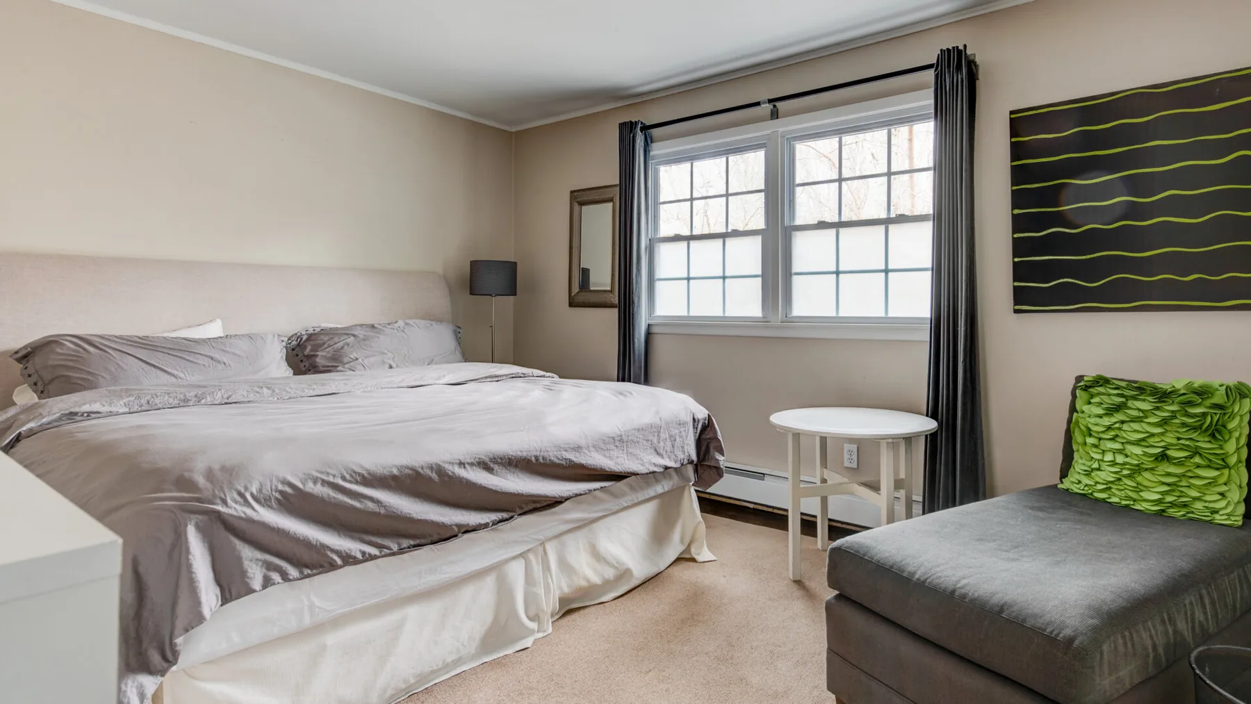 A bedroom with a bed, a window, and a gray upholstered seat.