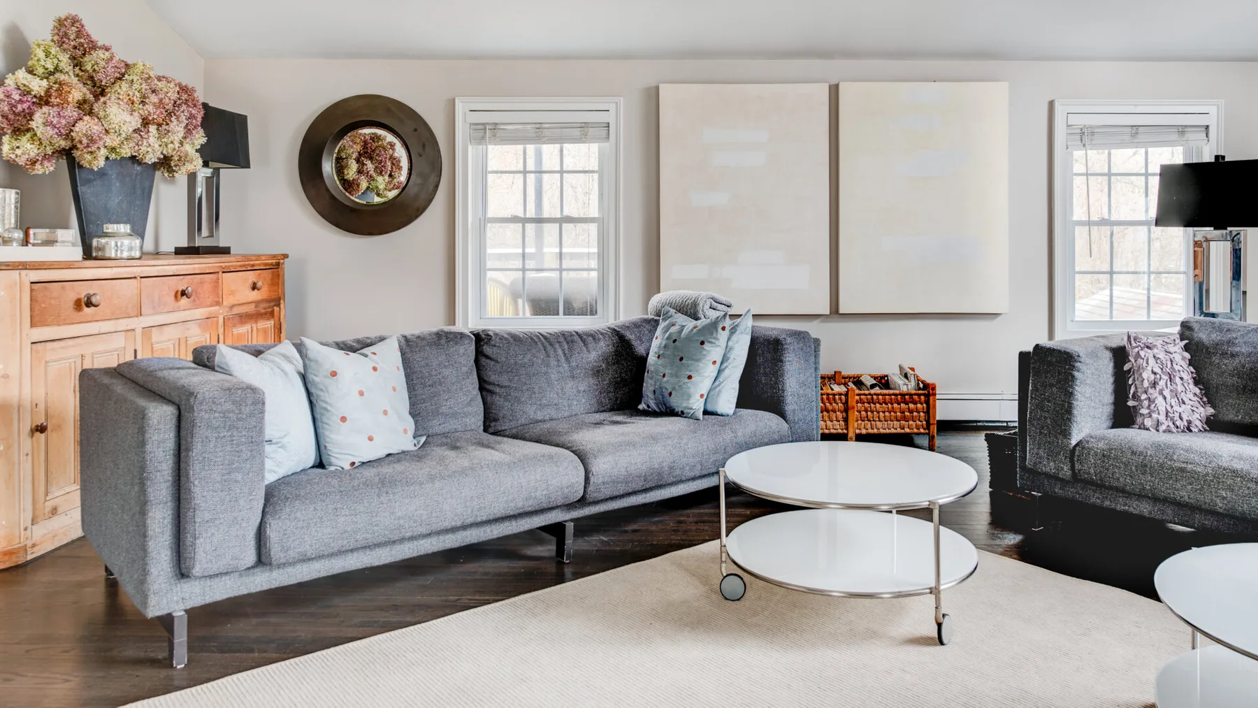 A living room with gray seating, a pair of round tables, and framed artwork.