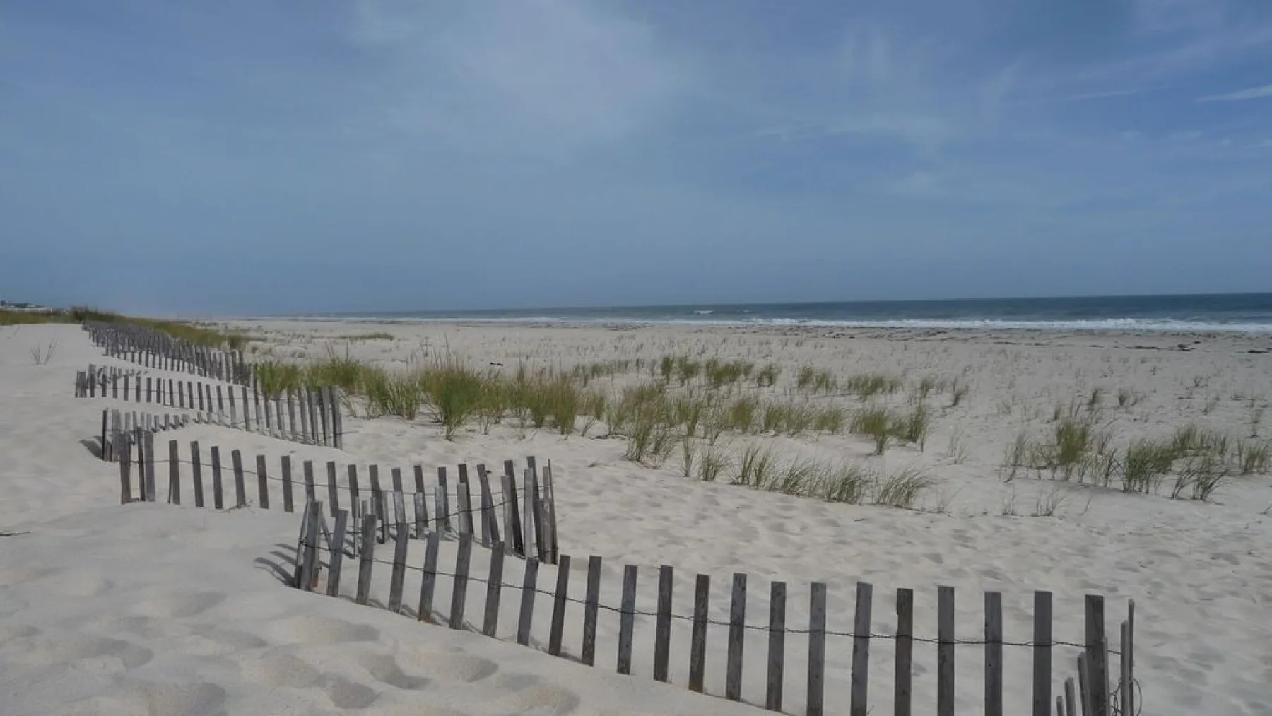 A sandy beach with low wooden fencing and grassy dunes beside the water.