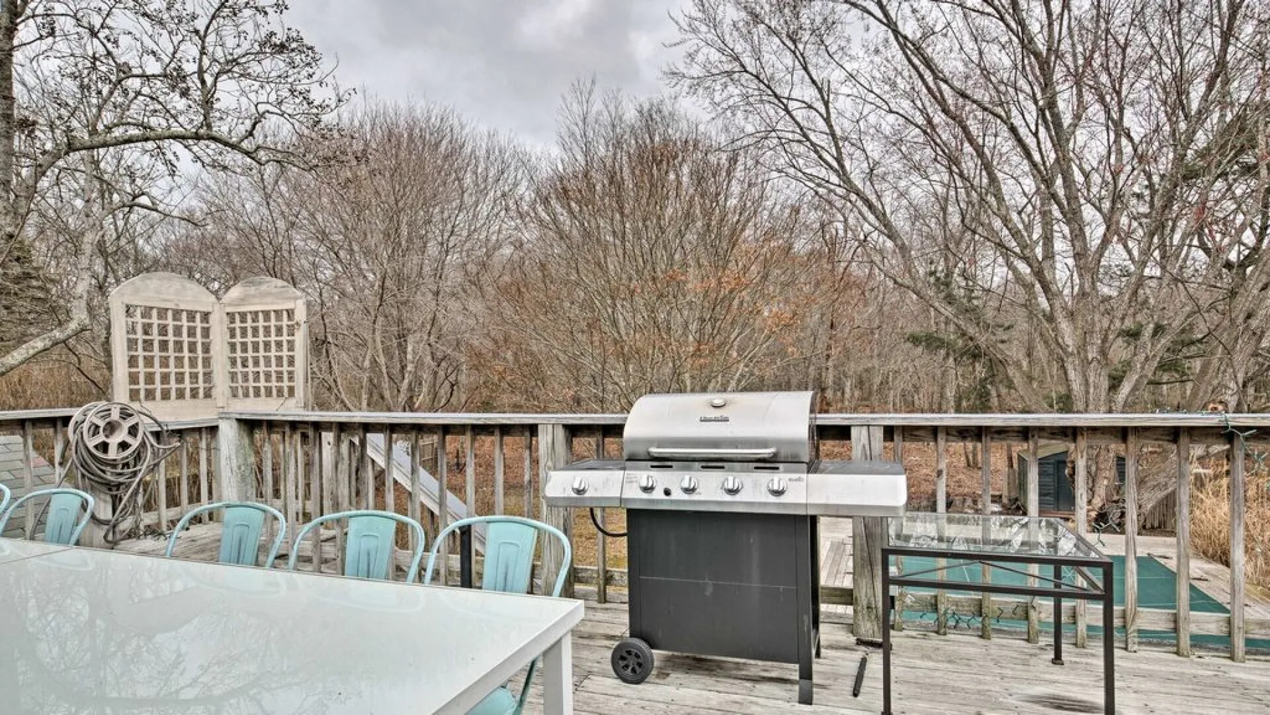 An outdoor deck with a grill, table, and seating overlooks leafless trees.