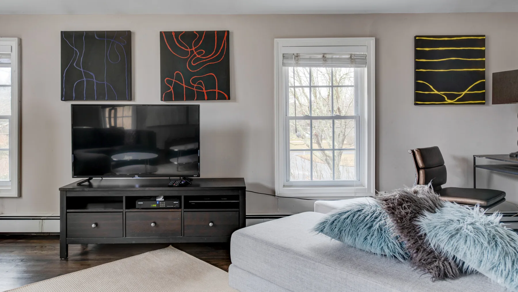 A living room with a television, wall art, and a light-colored sofa.