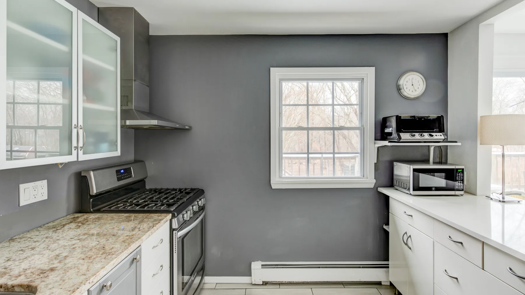 A kitchen with gray walls, white cabinets, and a window above the counter.