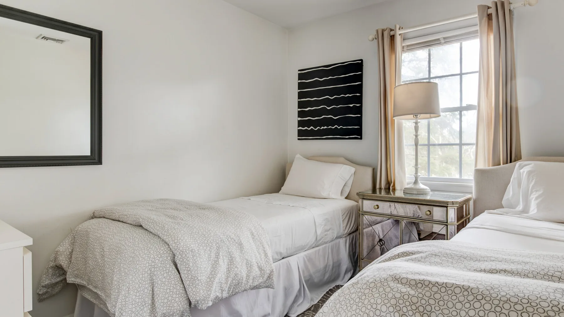 A bright bedroom with two single beds and a window dressed with curtains.