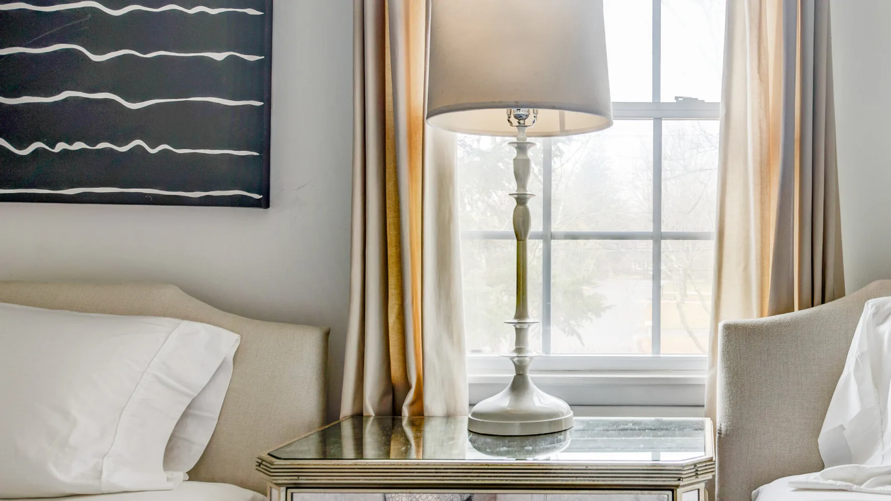 A bedroom seating area with a lamp on a table beside a bright window.