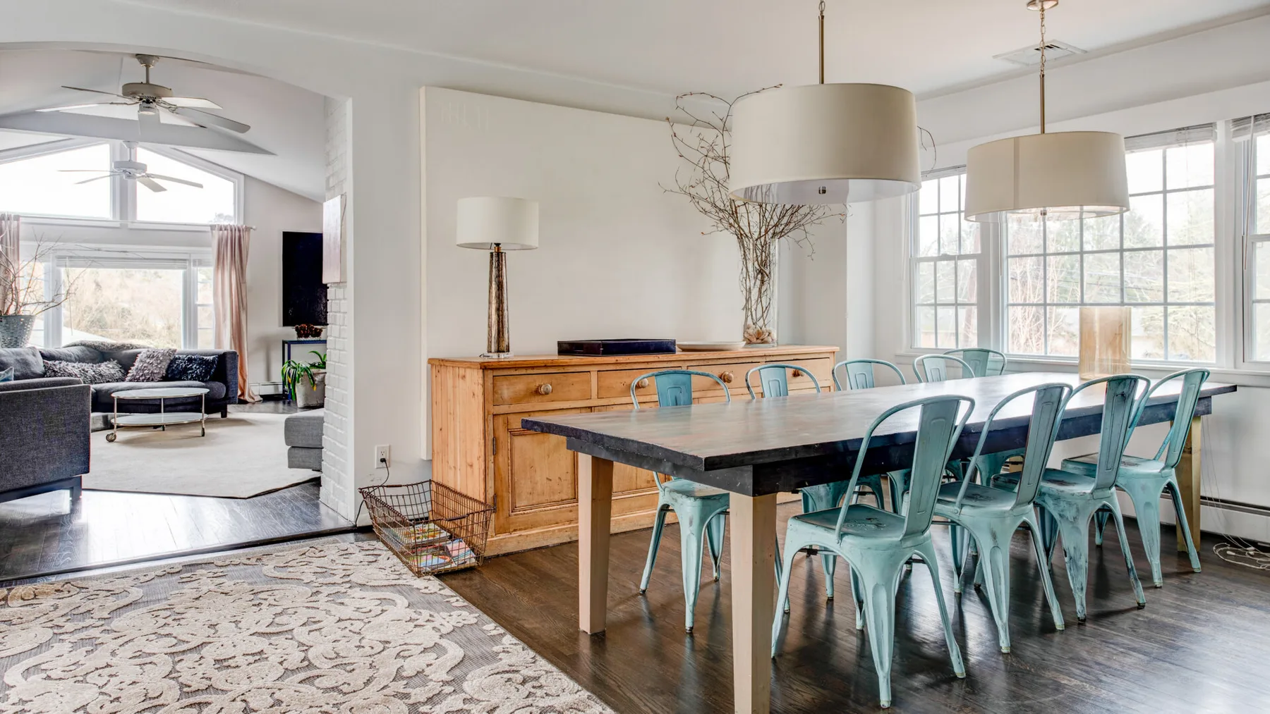 A dining area with a long table and teal seating beside large windows.