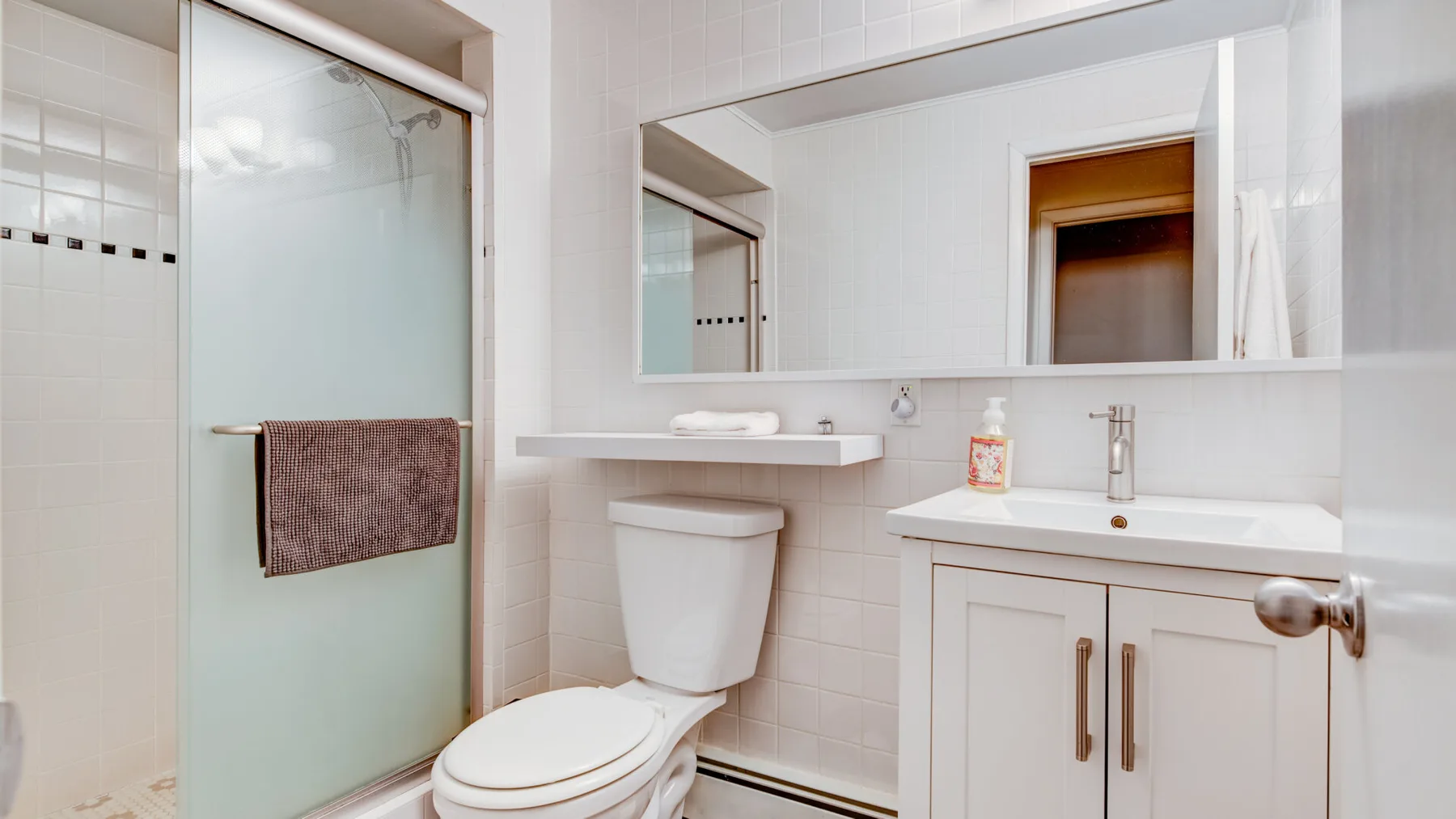 A bathroom with a glass shower, toilet, and vanity beneath a wide mirror.