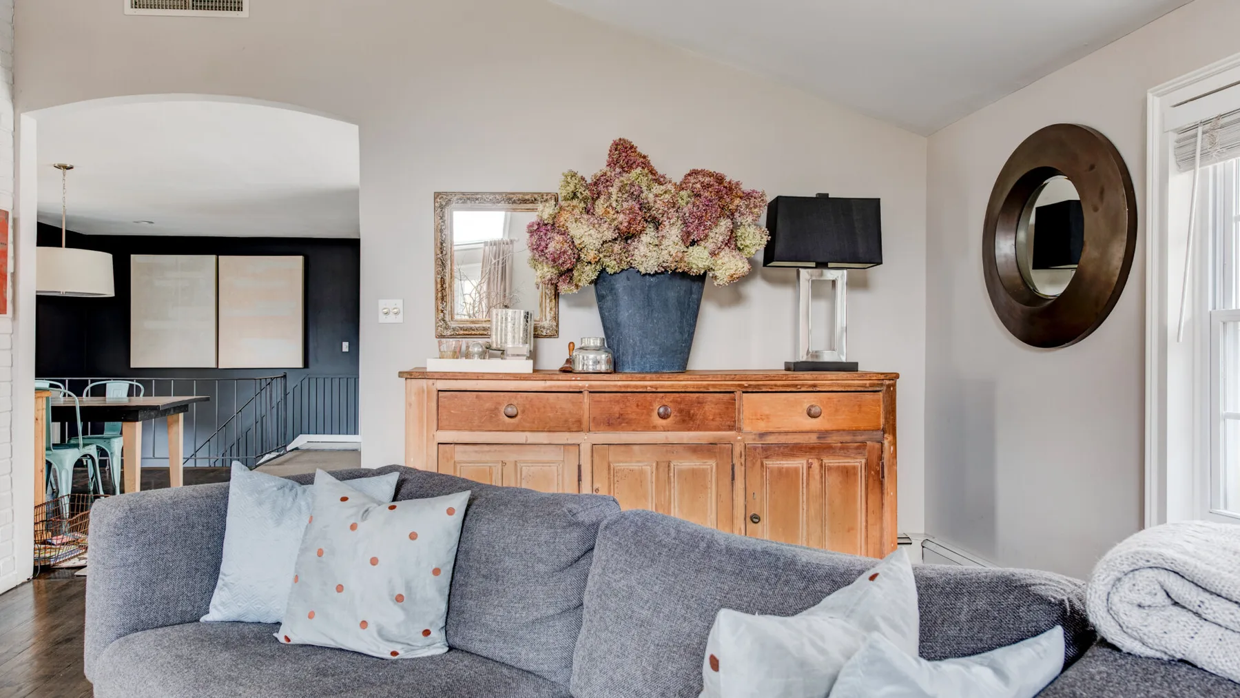 A living room with gray seating and a wooden console topped with flowers.