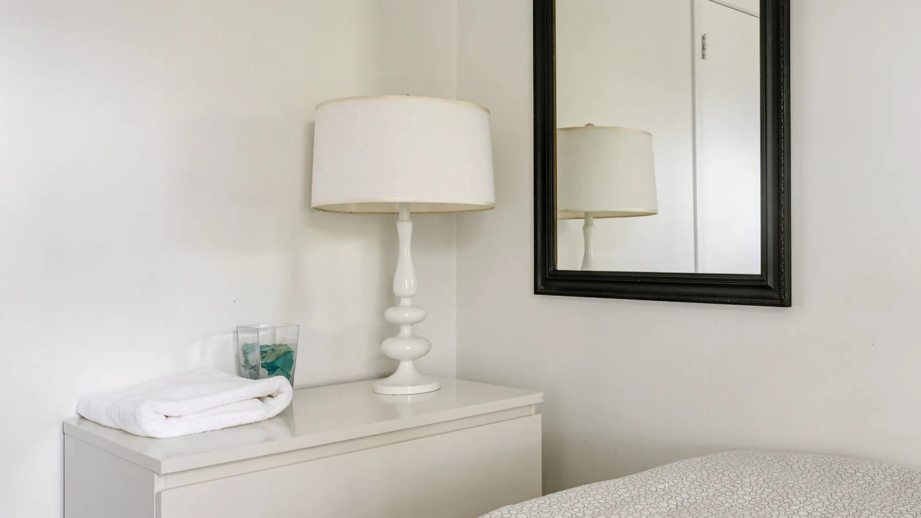 A room corner with a dresser, table lamp, and wall mirror.