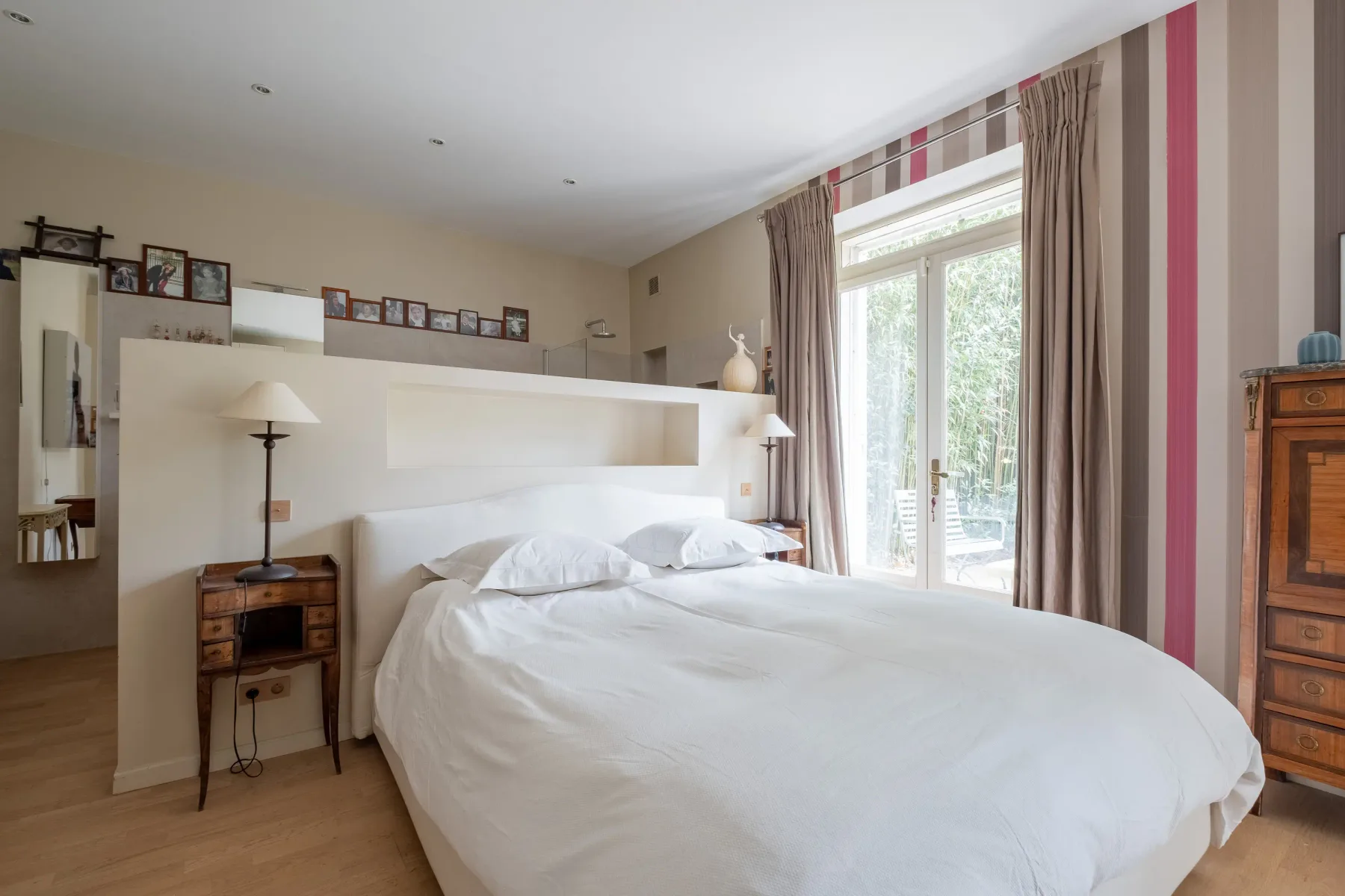 Un dormitorio con una cama bien hecha junto a ventanas altas con cortinas.