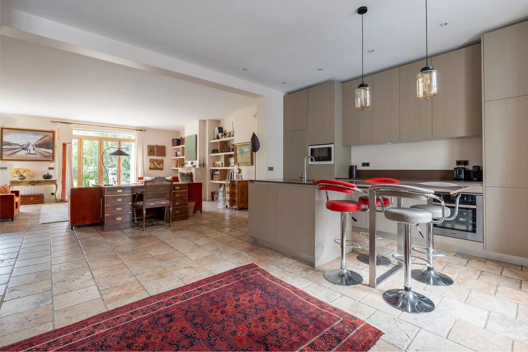 Una cocina abierta con zona de comedor, escritorio, asientos de barra y una alfombra estampada.