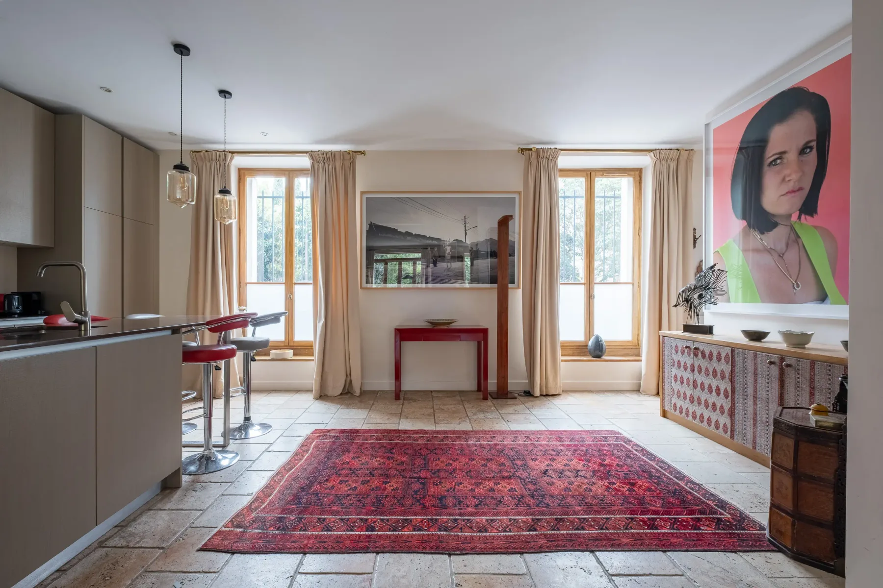 Una luminosa sala con comedor, una alfombra estampada y ventanas altas.