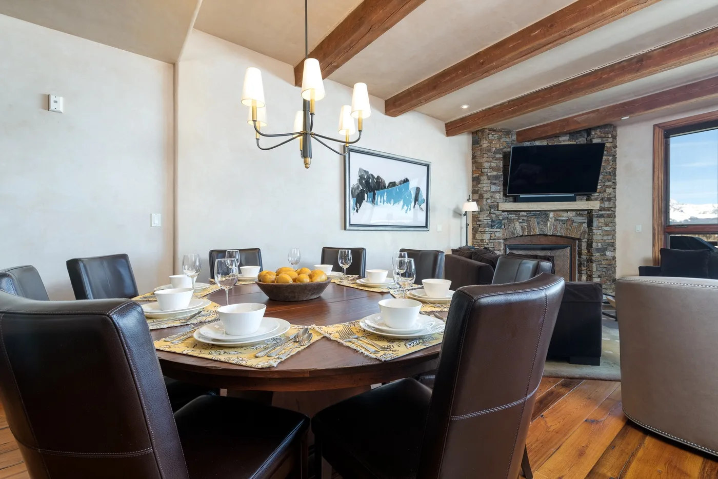 A dining area with a set table beside a stone fireplace and television.