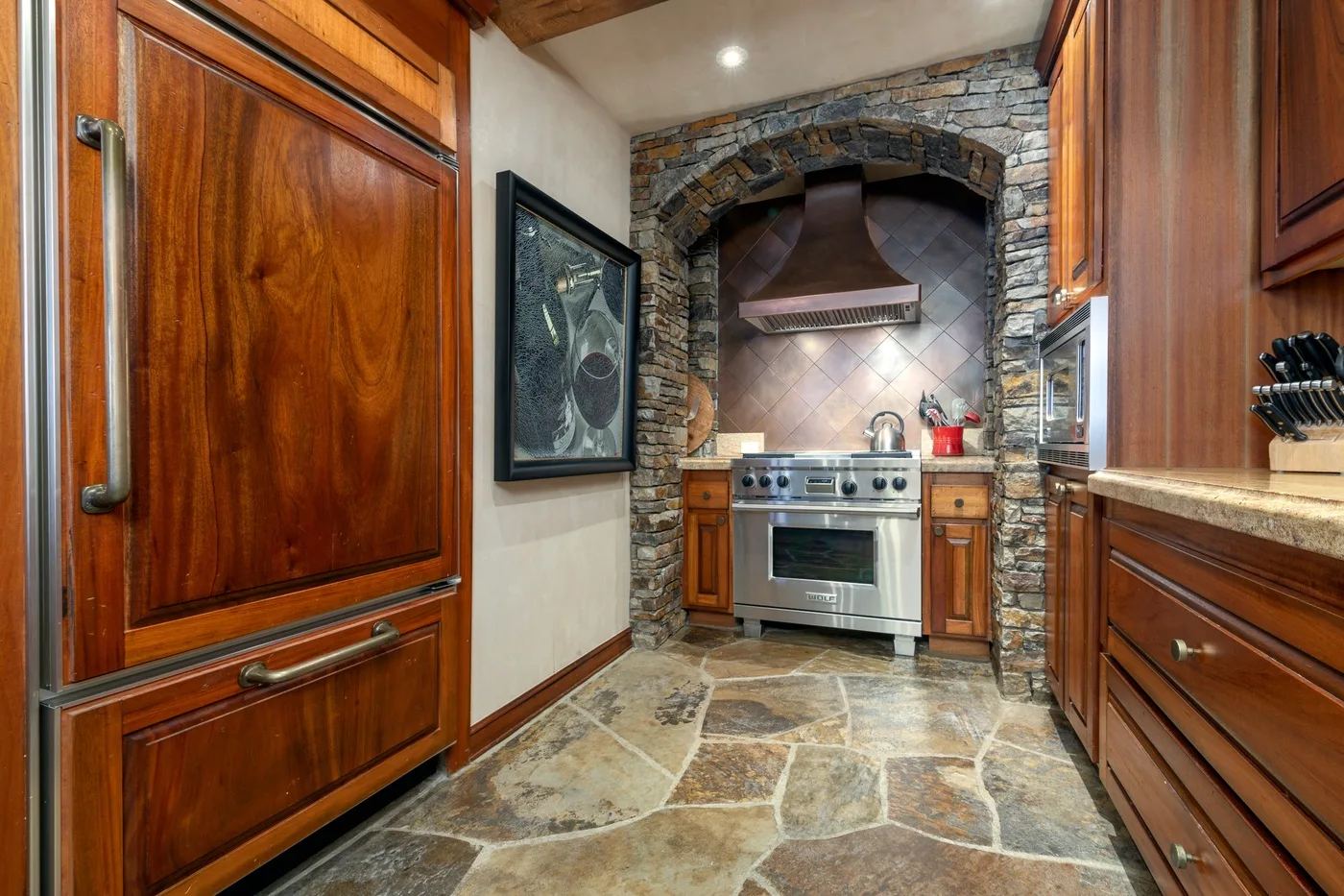 A kitchen with wooden cabinetry, a stainless steel range, and a stone arch.