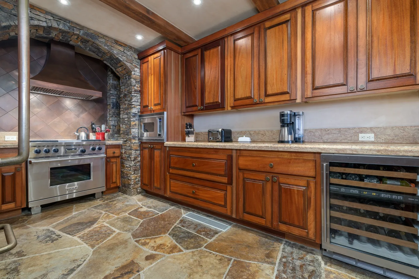 Una cocina con gabinetes de madera y una estufa bajo un arco de piedra.