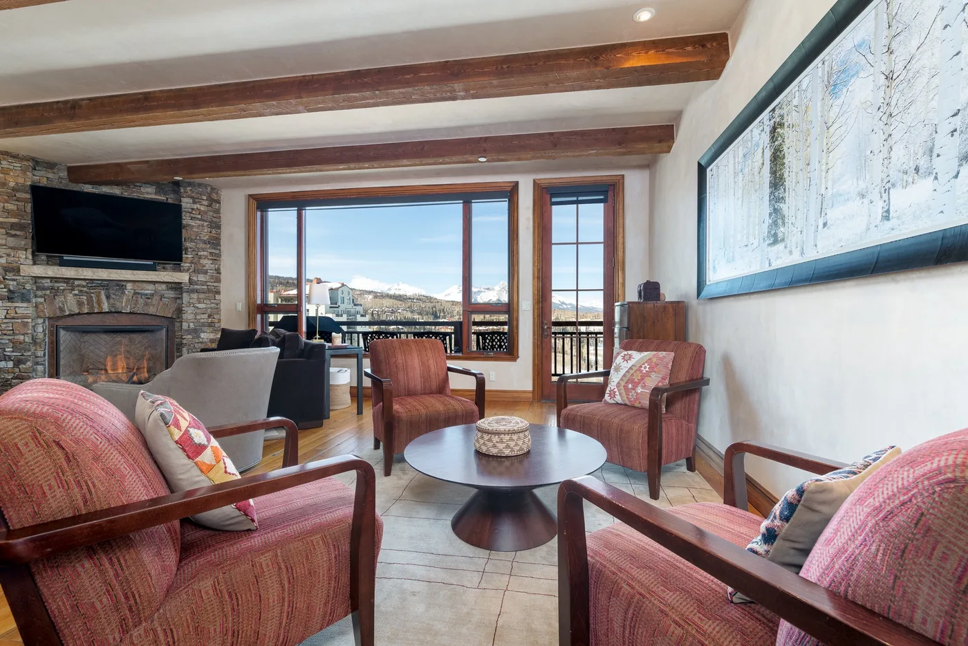 A living room with seating, a stone fireplace, and large windows overlooking the outdoors.