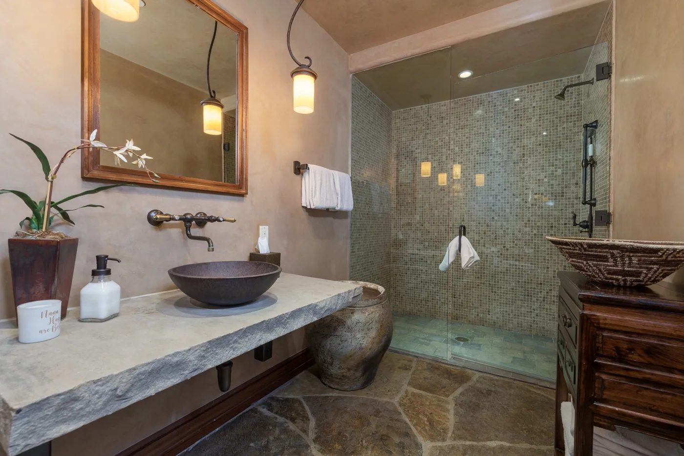 A bathroom with a stone counter, vessel sink, and glass-enclosed shower.