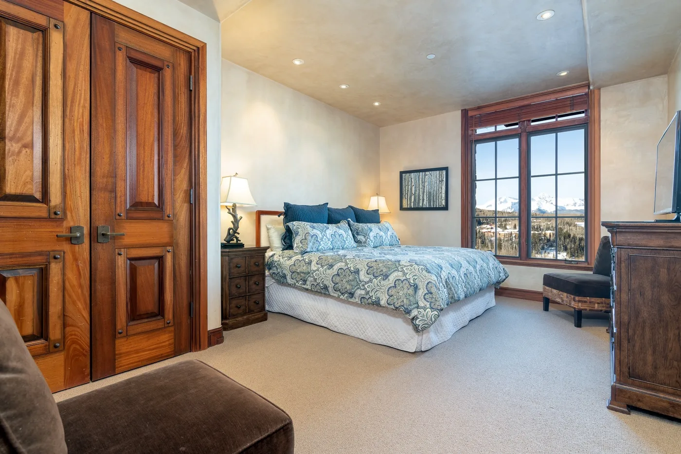 A bedroom with a bed beside a large window overlooking the landscape.