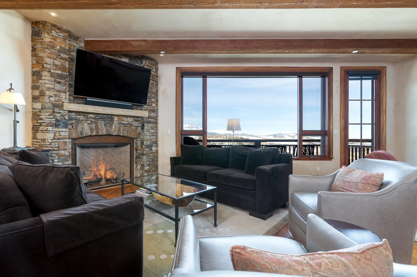A living room with seating arranged around a stone fireplace and large windows.