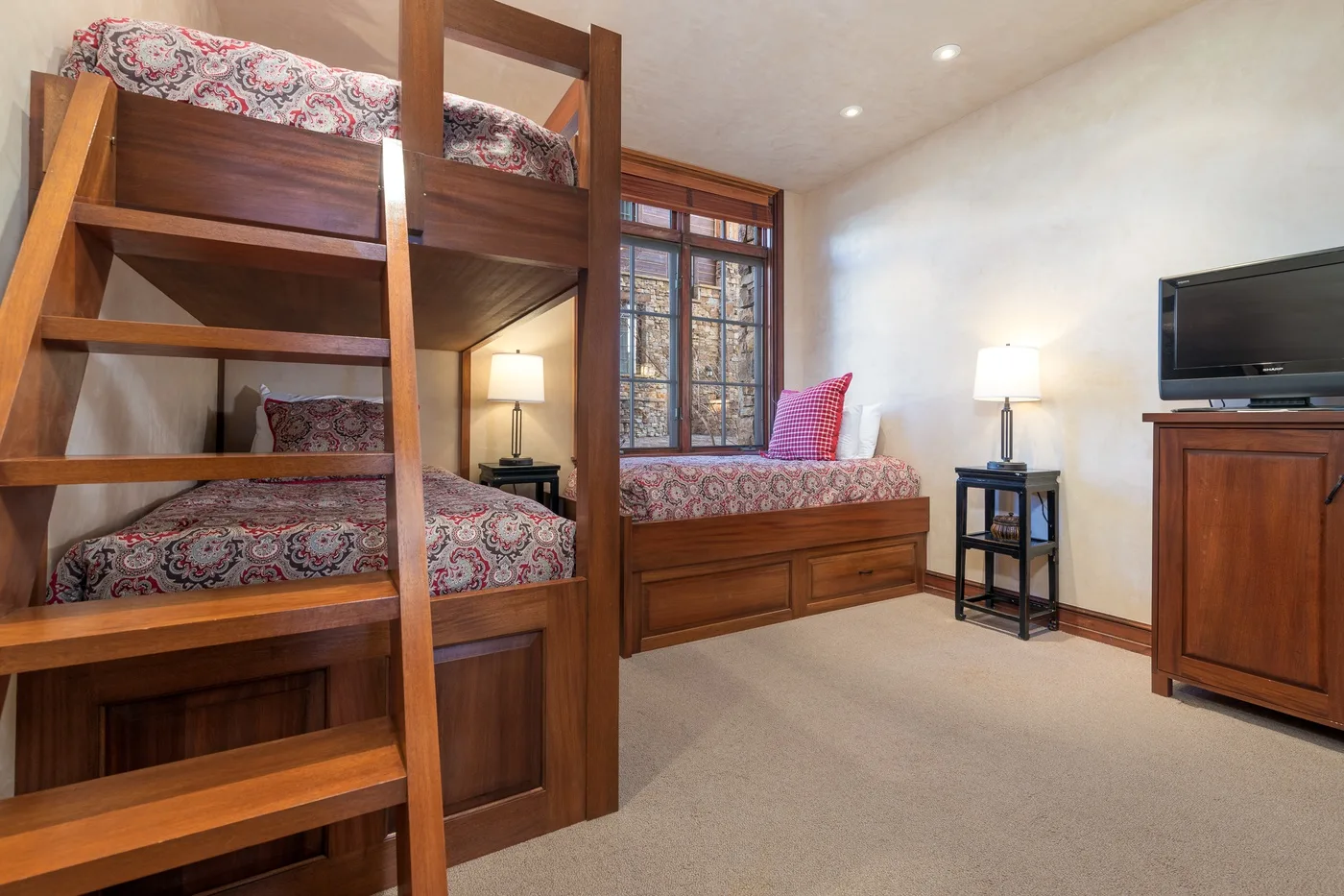 A bedroom with wooden bunk beds, a window, and a television.