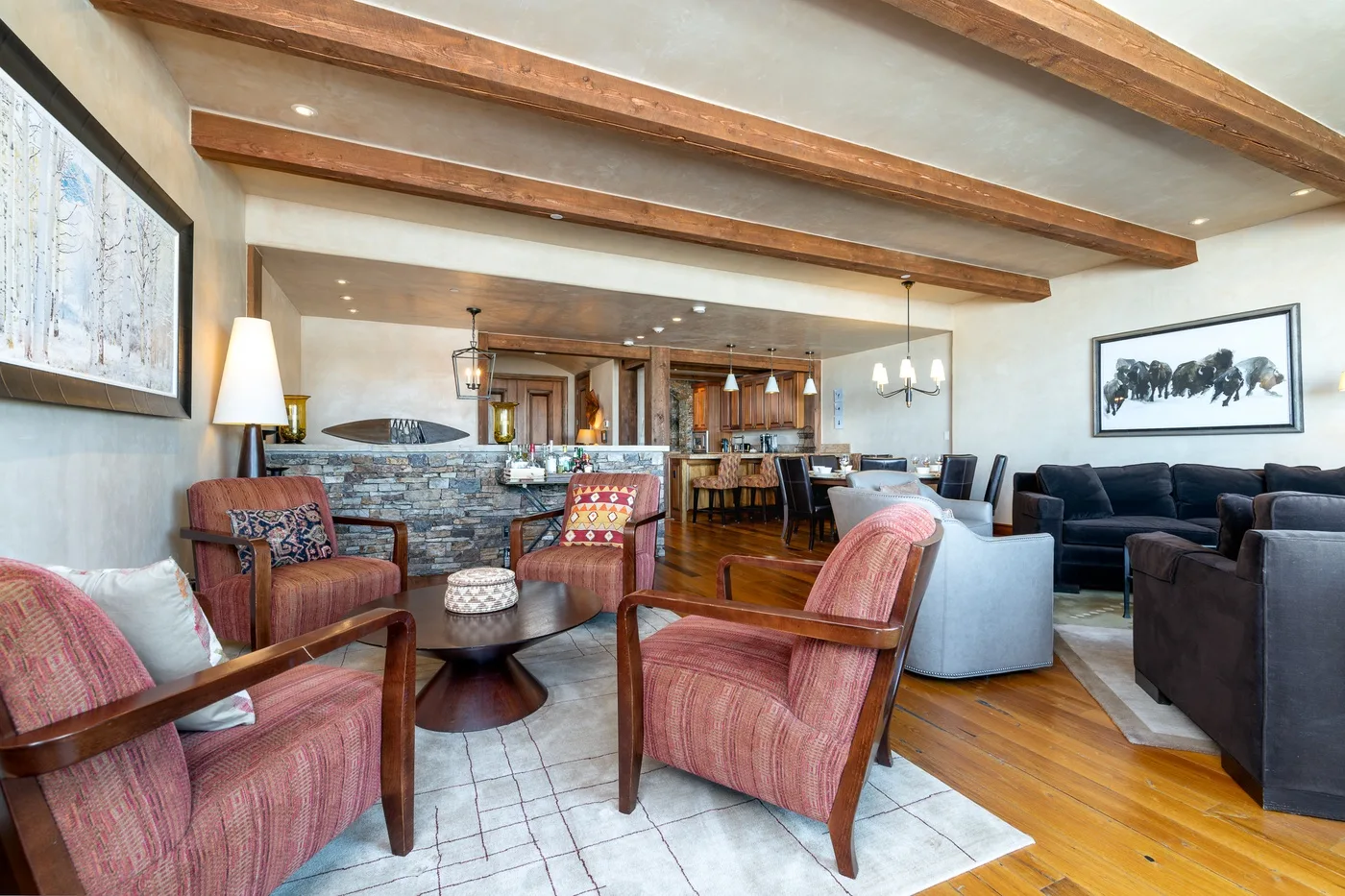 A living room with upholstered seating, a stone fireplace, and exposed ceiling beams.