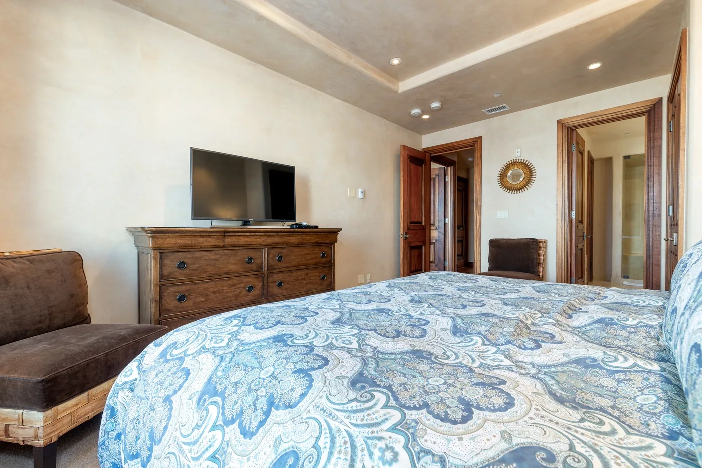 A bedroom with a bed covered in blue patterned bedding and a wooden dresser.