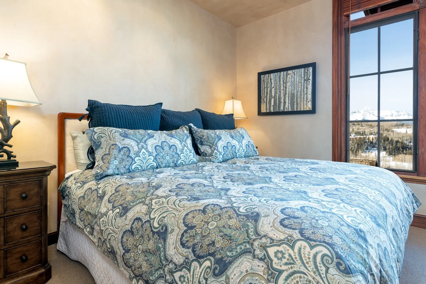 A bedroom with a large bed dressed in blue patterned bedding beside a tall window.