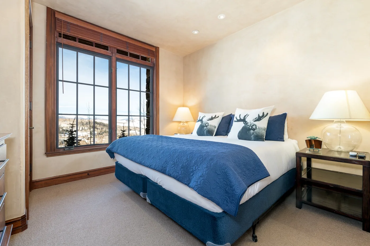 A bedroom with a blue-covered bed beside a large window.