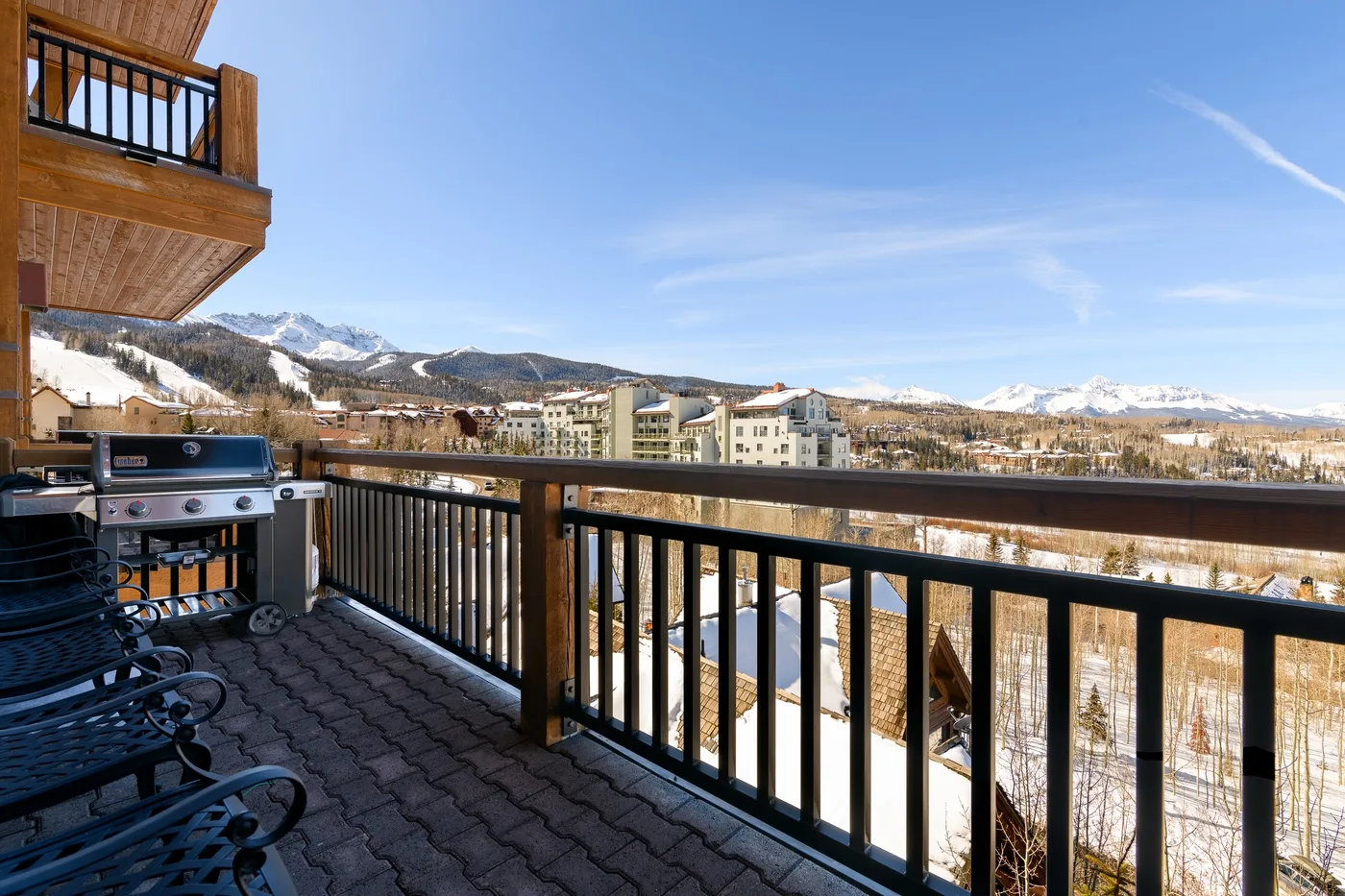 A balcony overlooks a snowy mountain landscape, with seating and a barbecue grill.