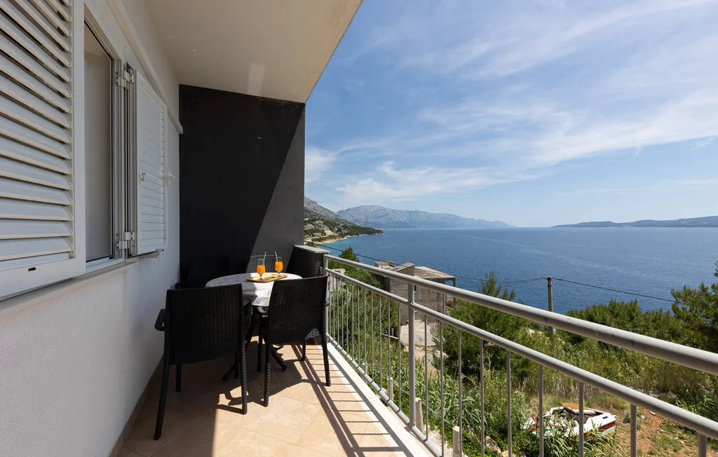 A balcony with outdoor seating overlooks the sea and distant coastline.