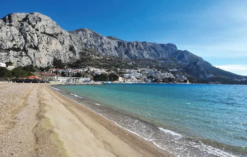 Una playa de arena bordea aguas azules y claras bajo una costa montañosa rocosa.